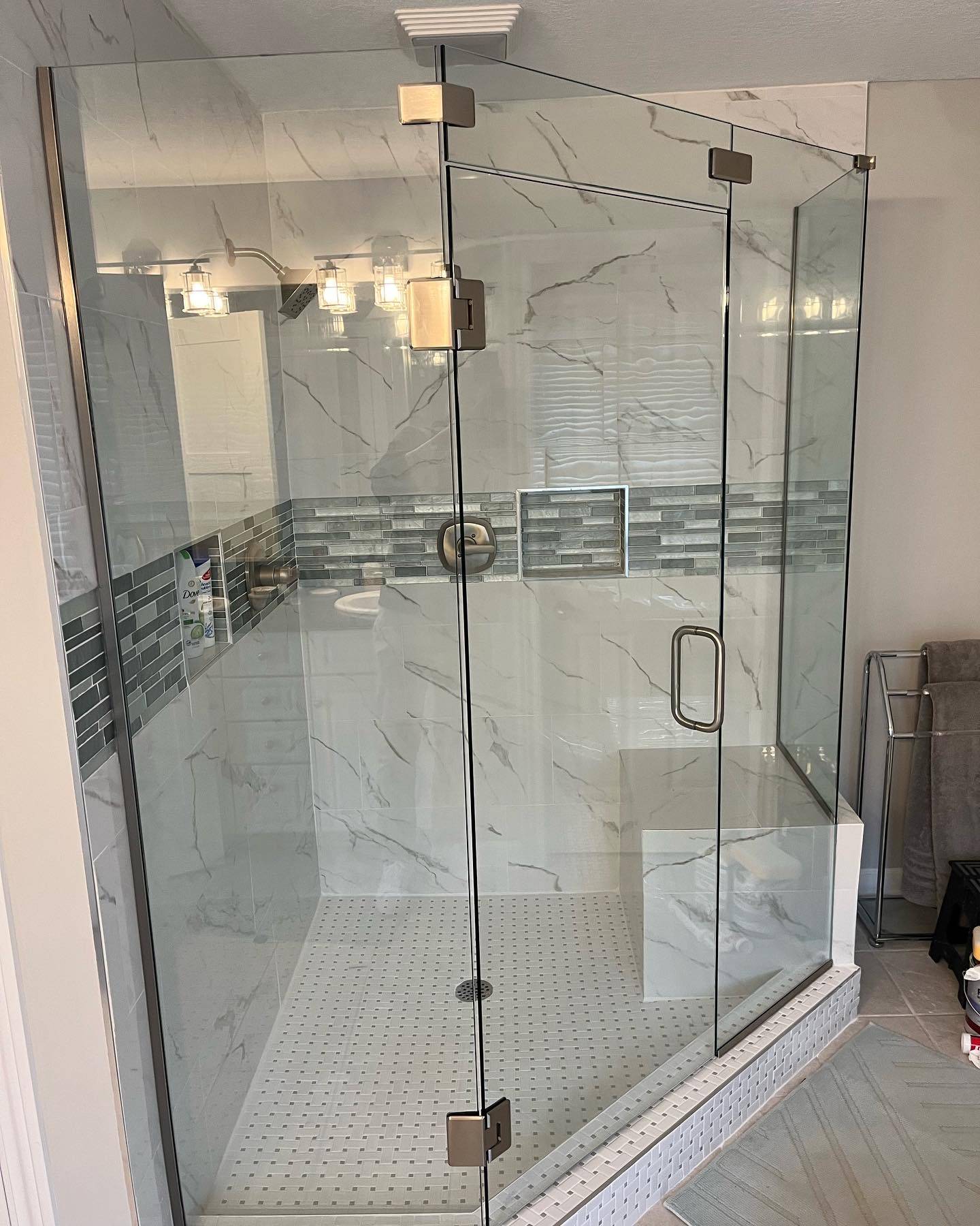 Walk-in shower with a frameless glass enclosure, marble-look wall tile and a glass mosaic accent band in a remodeled bathroom