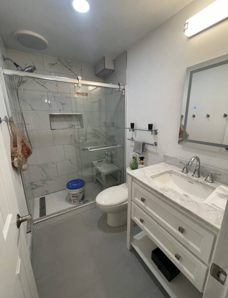 Remodeled bathroom with marble look tile shower, glass enclosure, and stone top vanity
