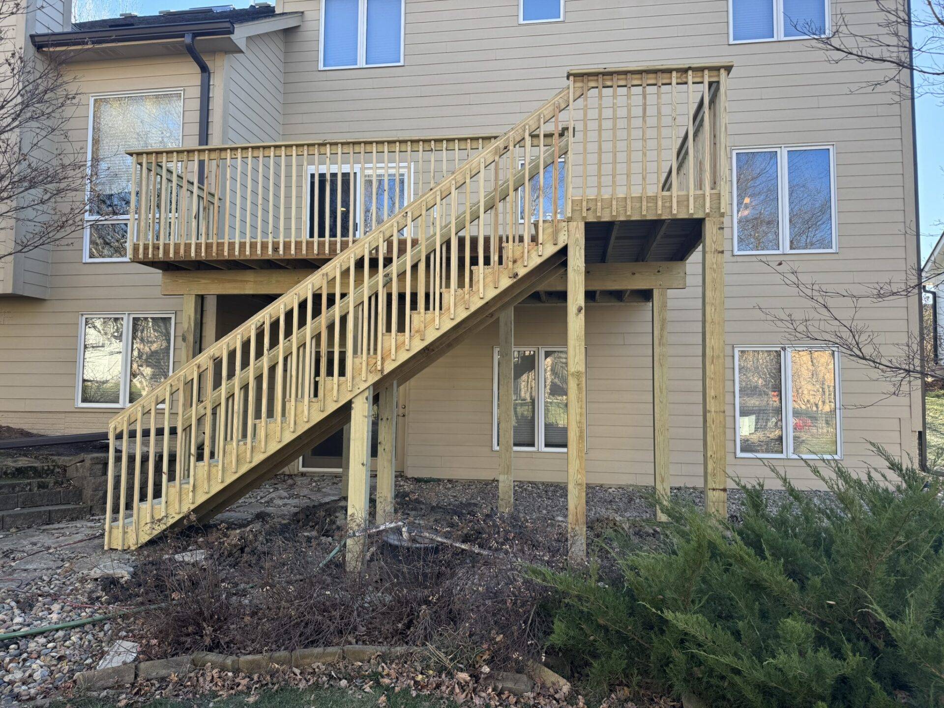 New raised pressure-treated wood deck with a long stair run down to grade on a two-story Central Iowa home, deck building project