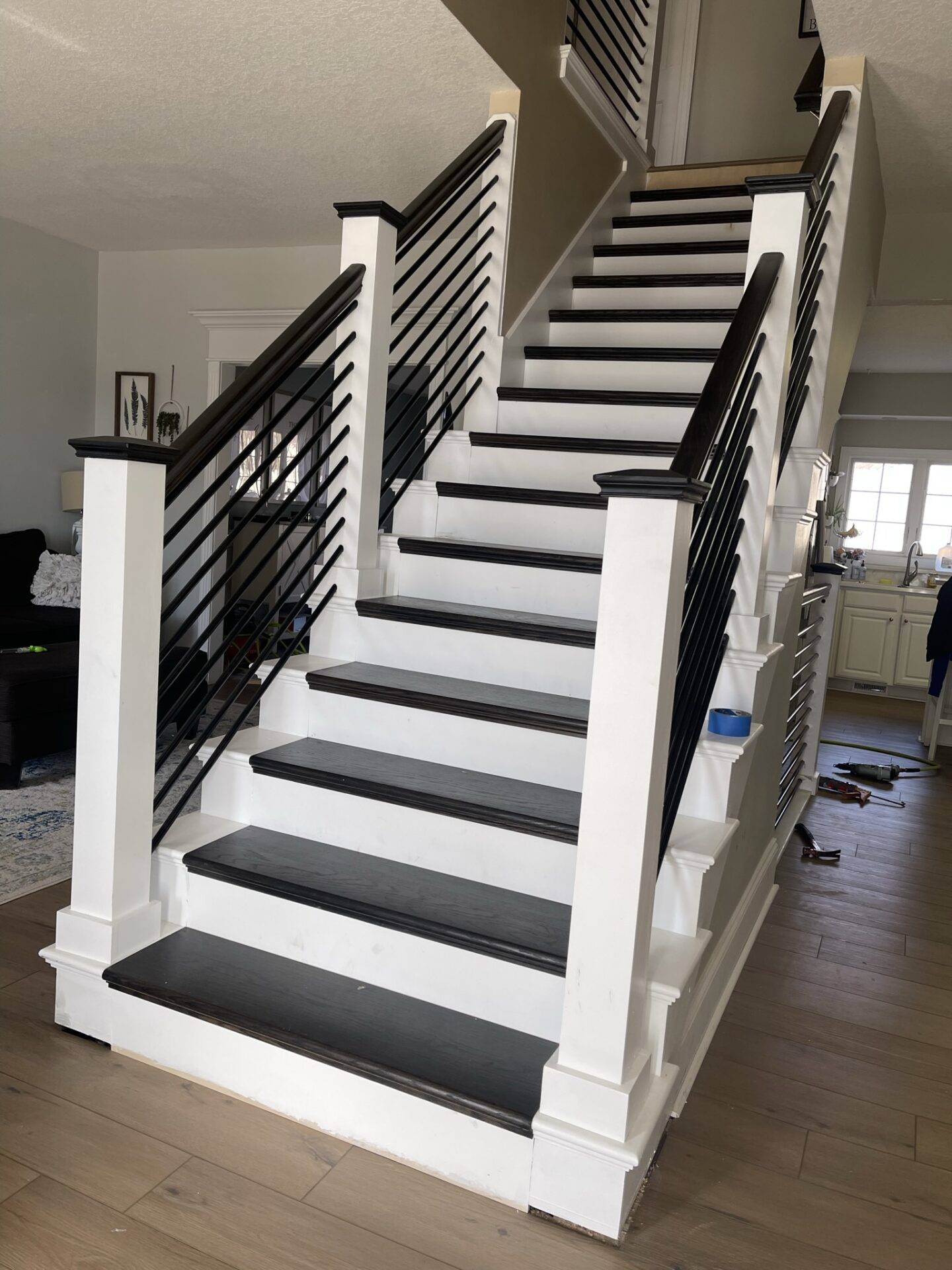 Remodeled staircase with dark stained treads, white risers and posts, horizontal black metal balusters and light plank flooring, whole-home remodel in Central Iowa