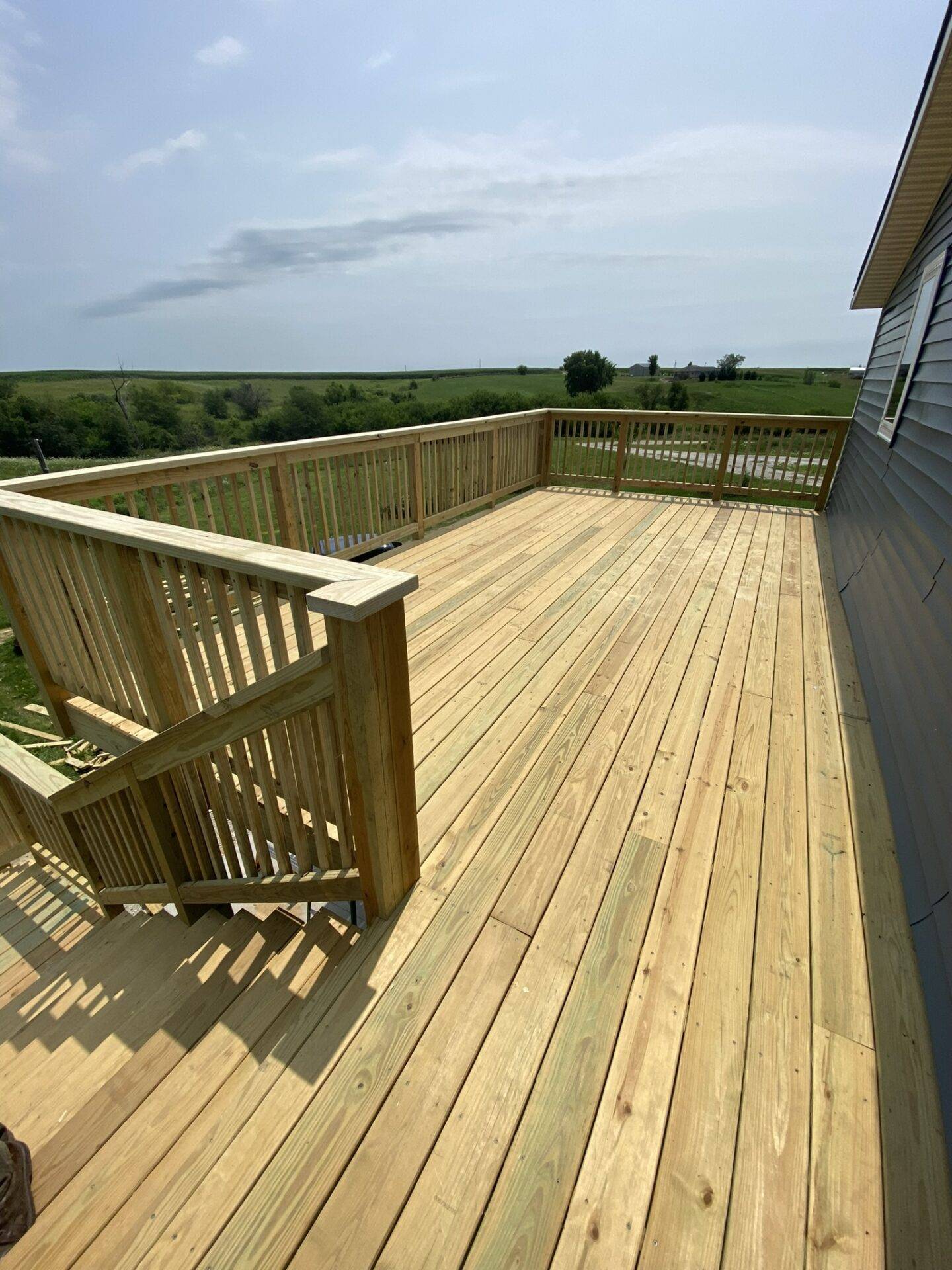 Fresh pressure-treated wood deck boards and railing on a Central Iowa home overlooking open farmland after deck building