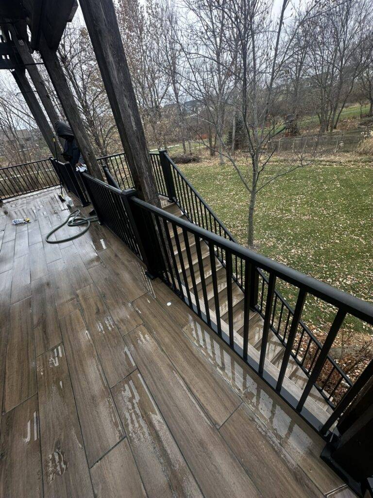 Composite deck boards with black metal railing overlooking a wooded backyard in Central Iowa