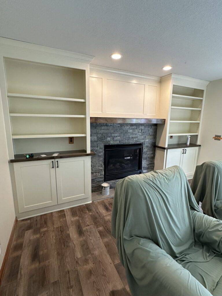 Interior remodel with custom white built-in cabinetry and shelving flanking a stone fireplace