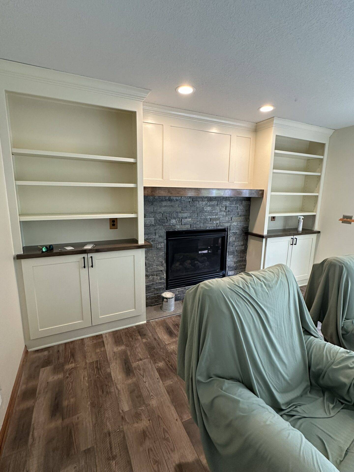 Interior home remodel with white built-in cabinets and shelves around a stacked-stone fireplace and wood mantel, furniture under drop cloths, Central Iowa