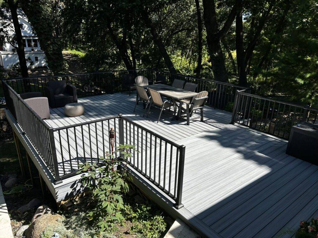 Finished composite deck with black metal railings and patio furniture in a wooded Iowa backyard
