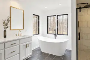 Illustration of a bathroom with a freestanding soaking tub, black frame windows, white shaker vanity and dark tile floor