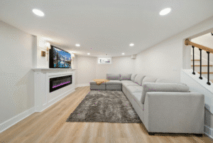 Busy Builders rendering of a finished basement family room with electric fireplace, wall-mounted TV, gray sectional sofa, and luxury vinyl plank flooring
