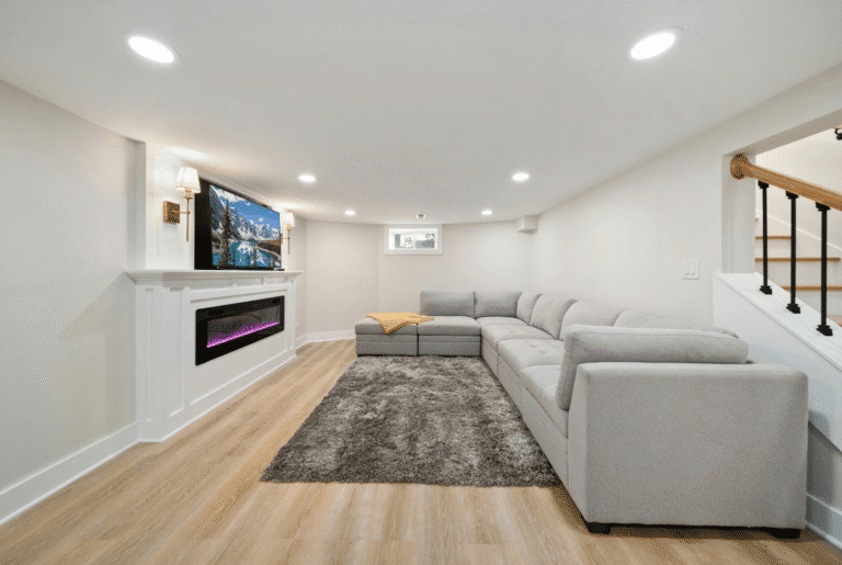 busy builders rendering of a finished basement family room with electric fireplace, wall-mounted tv, gray sectional sofa, and luxury vinyl plank flooring