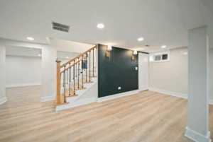 Finished basement with luxury vinyl plank flooring, dark green accent wall, gold wall sconces, recessed lighting, and open oak stair railing