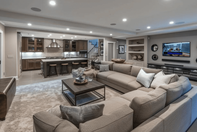 Busy Builders rendering of a finished basement open plan layout with large sectional sofa, built-in shelving, wall-mounted TV, and full wet bar with dark wood cabinetry and kitchen island