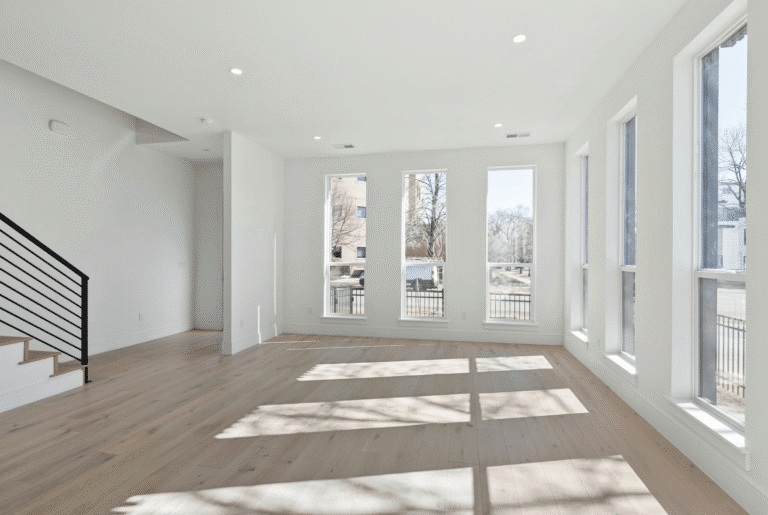 Busy Builders rendering of a home remodeling empty living room with wide plank hardwood flooring, recessed lighting, tall vertical windows, and natural light