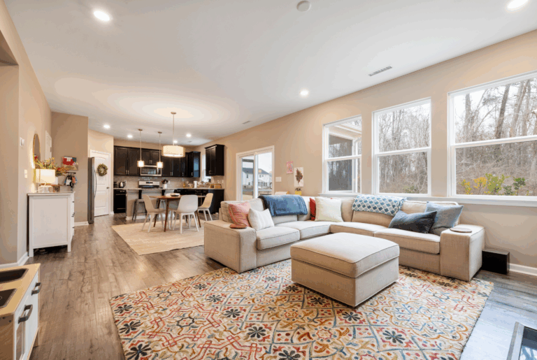 busy builders rendering of a home remodeling open plan living room with sectional sofa, hardwood flooring, large windows, and dark cabinetry kitchen visible in background