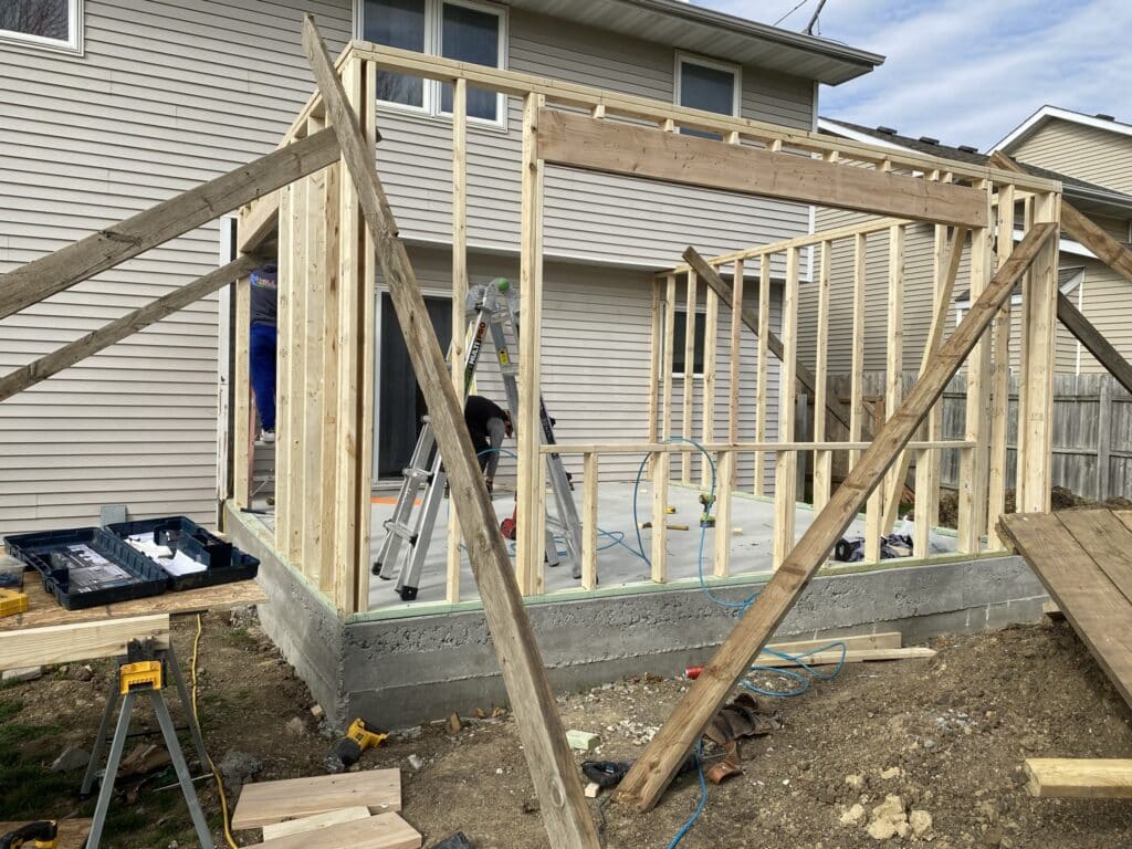 Home addition framing construction with new concrete foundation, wood stud wall framing, and crew working on existing Central Iowa home