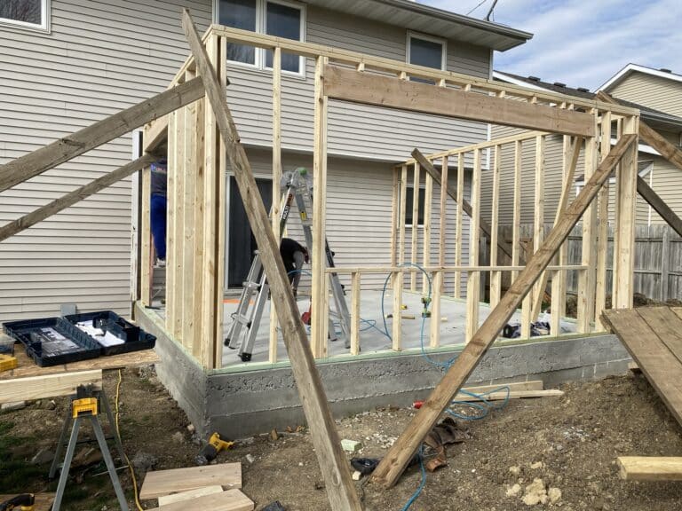 Home addition framing construction with new concrete foundation, wood stud wall framing, and crew working on existing Central Iowa home