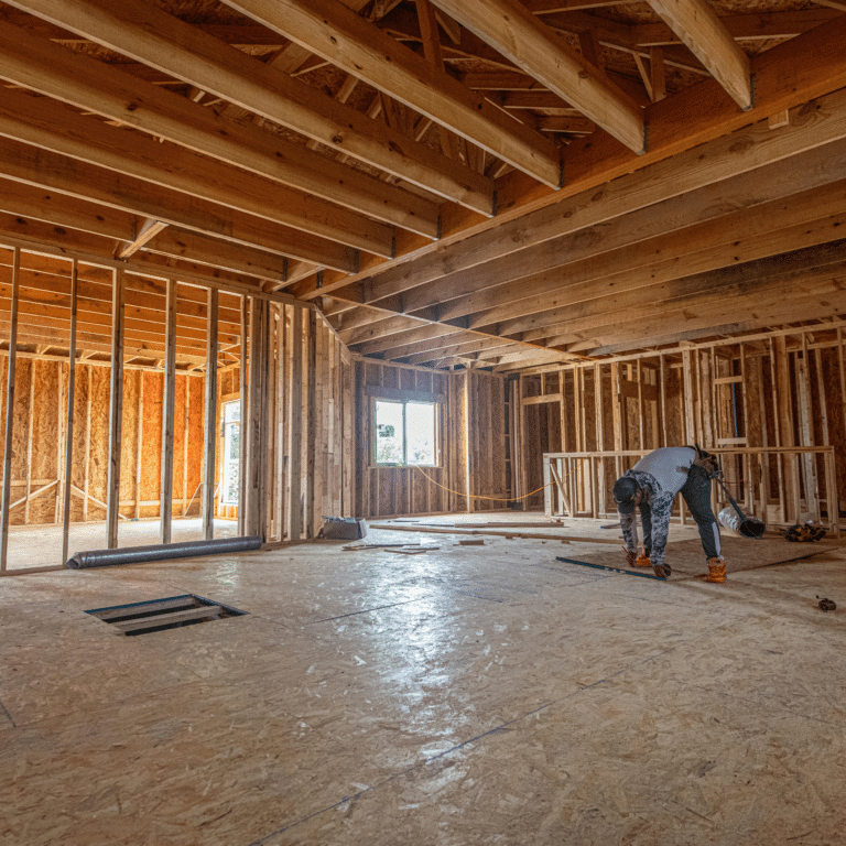 new home construction interior framing with open plan vaulted ceiling, osb subfloor, exterior wall sheathing, and crew working on framing layout