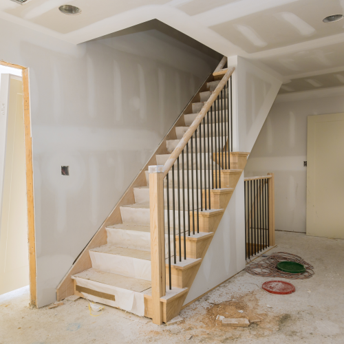 Home remodeling staircase installation with oak treads, black iron balusters, and wood newel posts during active construction with drywall complete