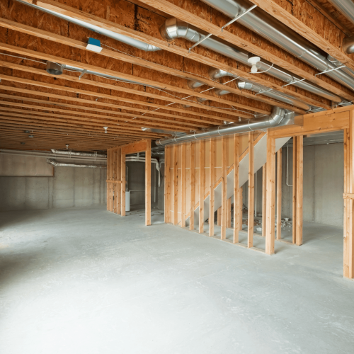 Basement finishing framing with exposed metal HVAC ductwork, staircase rough framing, and concrete foundation walls in an unfinished Central Iowa basement